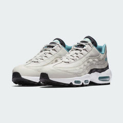 Angled view of two Nike Air Max 95 Essential Men's running shoes in beige, turquoise, and black, side by side, showcasing their timeless design and layered upper.