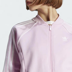 Close-up zoom on the fabric of the Adidas Adicolor Classics Superstar Track Jacket in pink, showing the soft texture and the embroidered Adidas Trefoil logo detail on the chest.