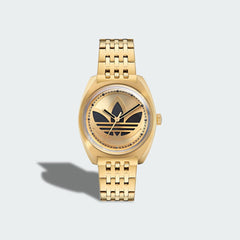 Adidas Edition One Watch in gold metallic, front view showing the watch face with a large, cut-through Trefoil logo and a domed lens.