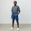 Person wearing a gray t-shirt and blue shorts standing against a plain background