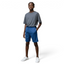 Person wearing a gray t-shirt and blue shorts standing against a plain background