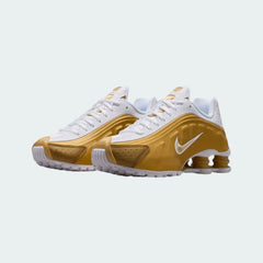 Angled view of two Nike Shox R4 Juniors' trainers in white and metallic gold, side by side, showcasing their bold, tech-inspired design.