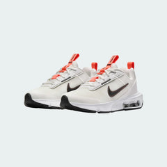 Angled view of two Nike Air Max Intrlk Lite Juniors' trainers in off-white and black, side by side, showcasing their modern aesthetic and lightweight construction.