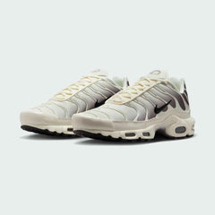 Angled view of two Nike Air Max Plus TN Men's trainers in beige and black, side by side, showcasing their bold design and layered construction.