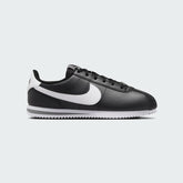 Nike Cortez Juniors' trainers in black with a white Nike Swoosh and white midsole, side profile showing classic silhouette.
