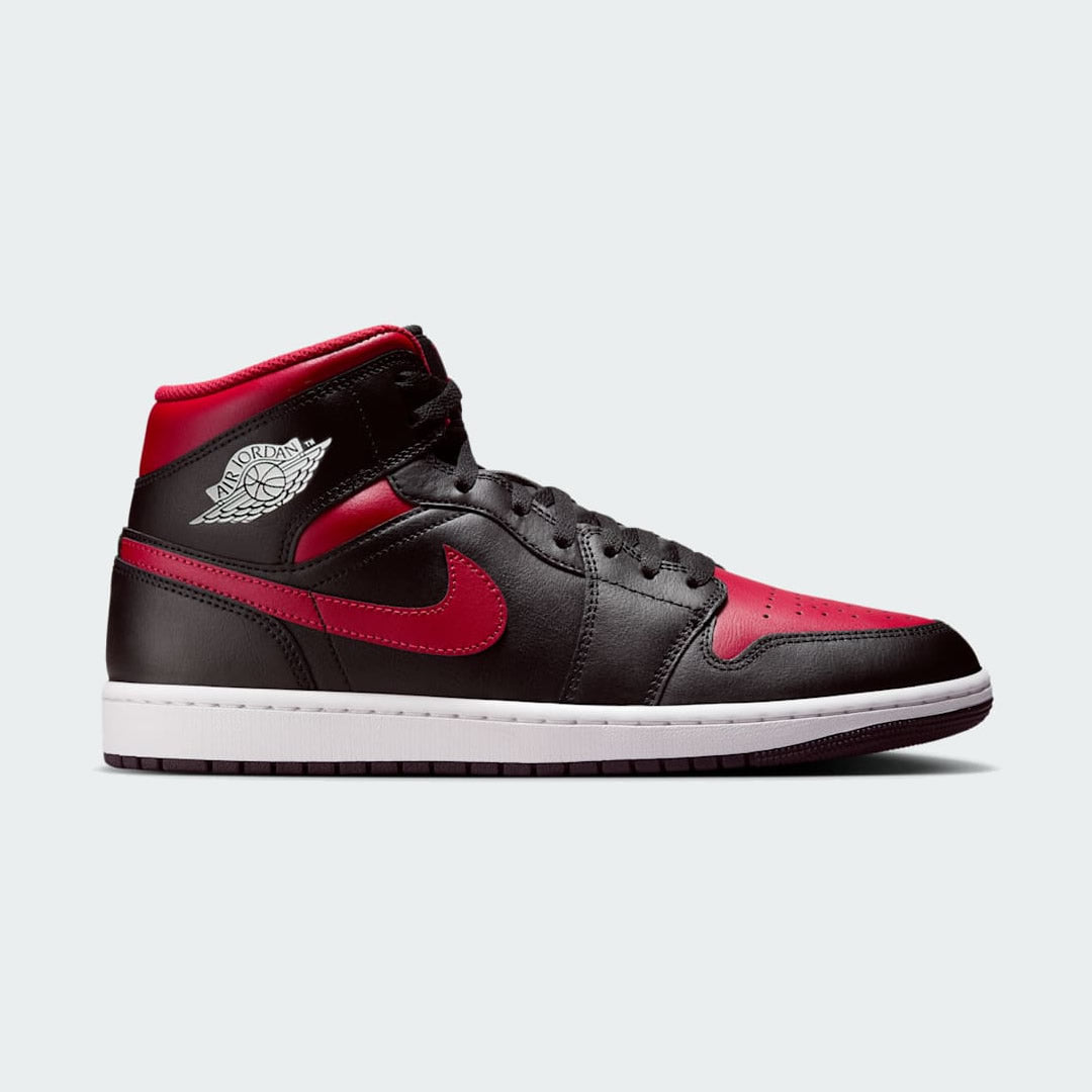 Air Jordan 1 Mid Men's trainers in black leather with red and white accents, side profile showing mid-cut silhouette, perforated toe box, and white Nike Swoosh.