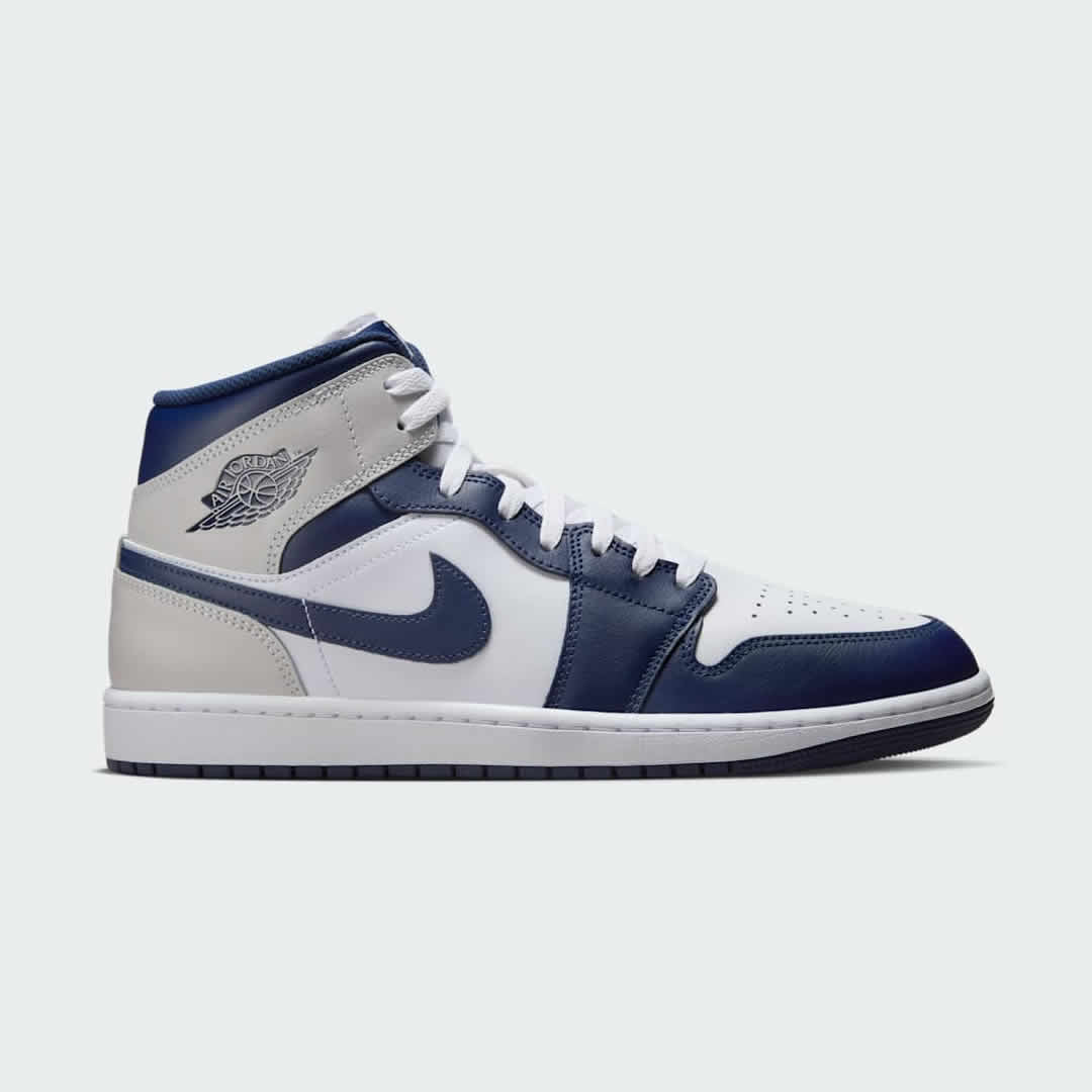 Air Jordan 1 Mid Men's trainers in white leather with royal blue and black accents, side profile showing mid-top design, classic Swoosh, and Wings logo.