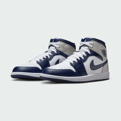 Angled view of two Air Jordan 1 Mid Men's trainers in white, royal blue, and black, side by side, showcasing their iconic design and bold colour blocking.