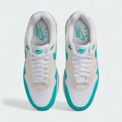 Top-down view of a pair of Nike Air Max 1 Women's trainers in white, blue-green, and grey, highlighting their classic silhouette and lace-up closure.
