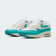 Angled view of two Nike Air Max 1 Women's trainers in white with blue-green accents, side by side, showcasing their timeless design and layered upper.