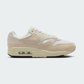 Nike Air Max 1 Women's trainers in sail off-white with guava ice pink and black accents, side profile showing visible Max Air unit in the heel and a layered leather upper.