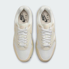 Top-down view of a pair of Nike Air Max 1 Women's trainers in off-white and pink, highlighting their classic silhouette and lace-up closure.