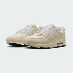 Angled view of two Nike Air Max 1 Women's trainers in sail, guava ice, and black, side by side, showcasing their timeless design and layered upper.