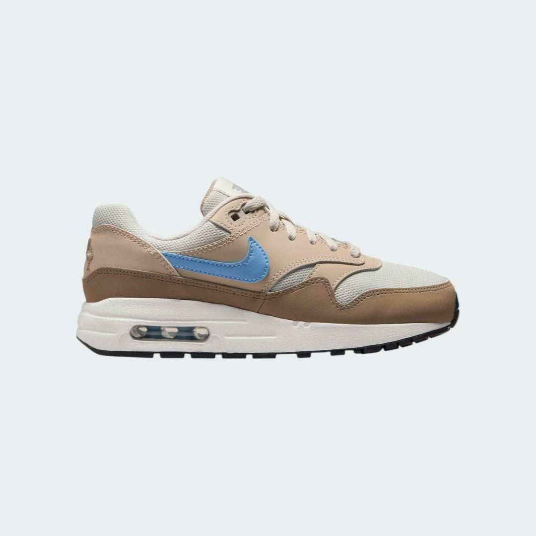Nike Air Max 1 Juniors' trainers in light bone brown with a psychic blue Swoosh, side profile showing visible Max Air unit in the heel and a layered leather upper.