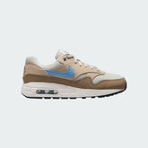 Nike Air Max 1 Juniors' trainers in light bone brown with a psychic blue Swoosh, side profile showing visible Max Air unit in the heel and a layered leather upper.
