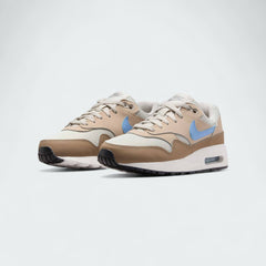Angled view of two Nike Air Max 1 Juniors' trainers in light bone, psychic blue, and black, side by side, showcasing their timeless design and layered upper.