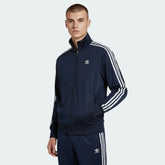 Adidas Firebird Track Jacket Men's in collegiate navy, front view showing full zip, stand-up collar, white 3-Stripes on sleeves, and Trefoil logo worn my model