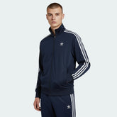 Adidas Firebird Track Jacket Men's in collegiate navy, front view showing full zip, stand-up collar, white 3-Stripes on sleeves, and Trefoil logo worn my model