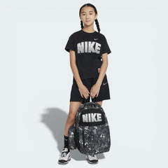 Person wearing a black Nike t-shirt and shorts, holding a black and white Nike backpack on a light gray background