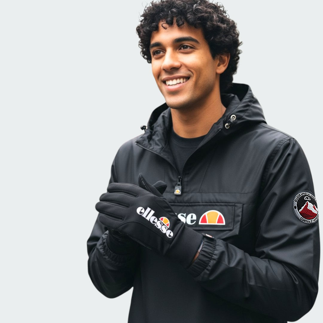 A hand wearing the Ellesse Daxo Touchscreen Glove in black, demonstrating its snug fit and the ability to use a smartphone with the glove on.