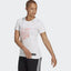 A woman wearing a white Adidas t-shirt with a graphic design, paired with black pants with a side stripe.