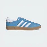 Side Profile Image: The Light Blue Gazelle Indoor, highlighting the Cloud White 3-Stripes and the distinctive translucent gum rubber outsole.