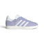 Displays the full lateral silhouette featuring the soft Violet Tone suede upper, contrasting Cloud White serrated 3-Stripes, gleaming metallic gold foil "Gazelle" lettering, matching white heel tab, and the clean rubber cupsole.