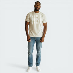 Man wearing a beige t-shirt and blue jeans on a white background