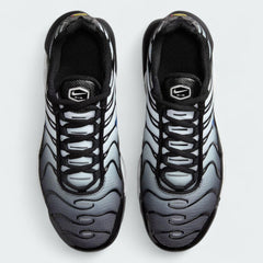 Top-down view of a pair of Nike Air Max Plus TN Juniors' trainers in white, blue, and black, highlighting their iconic silhouette and lace-up closure.