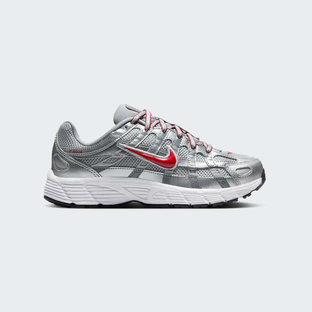 Nike P-6000 Juniors' trainers in metallic silver with gym red accents, side profile showing layered mesh and synthetic/leather overlays.