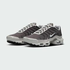 Angled view of two Nike Air Max Plus TN Men's trainers in brown and grey, side by side, showcasing their bold design and layered construction.