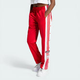 Side profile of the Better Scarlet Adibreak pants, highlighting the full-length white snap buttons and the contrast 3-Stripes.