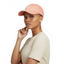 Person wearing a peach-colored cap with a brand logo on a light gray background
