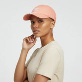Person wearing a peach-colored cap with a brand logo on a light gray background