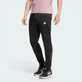 Side profile of the black Adidas training pants, highlighting the camouflage-print Three Stripes running down the leg.
