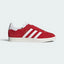 Highlights the high-velocity sweep of the white serrated 3-Stripes and the professional, gleaming depth of the metallic gold foil Gazelle branding against the Better Scarlet suede.