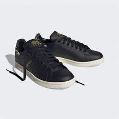 Angled view of two Adidas Stan Smith Women's black leather trainers with leopard print details, side by side, showcasing their timeless design with a bold twist.