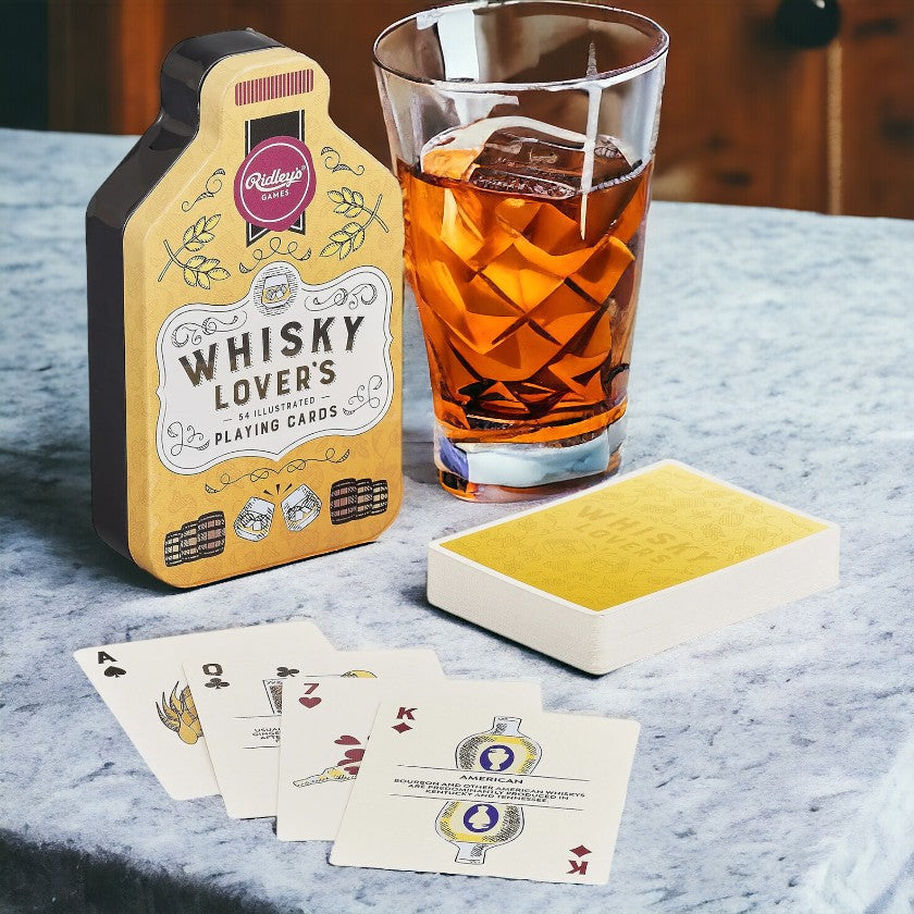 A set of playing cards displayed next to a glass of whisky, with the packaging indicating that the set is themed around whisky.