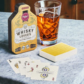 A set of playing cards displayed next to a glass of whisky, with the packaging indicating that the set is themed around whisky.