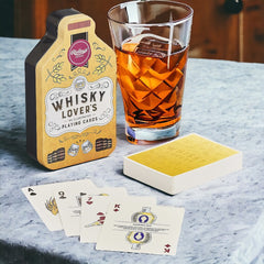 A set of playing cards displayed next to a glass of whisky, with the packaging indicating that the set is themed around whisky.