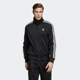 Adidas Firebird Track Jacket Men's in black, front view showing full zip, stand-up collar, white 3-Stripes on sleeves, and embroidered Trefoil logo.
