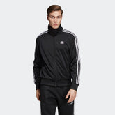 Adidas Firebird Track Jacket Men's in black, front view showing full zip, stand-up collar, white 3-Stripes on sleeves, and embroidered Trefoil logo.