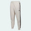 Nike Men's Tribute Woven Track Pants in light beige, front view showing elastic waistband, white side stripes/piping, and Nike Swoosh logo.