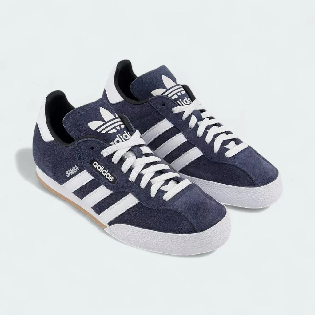 Angled view of two Adidas Samba Super Men's trainers in navy with white stripes and gum soles, side by side, showcasing their timeless design.