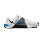 Medial side profile of the Nike Free Metcon 10 men's training shoe in a light grey and white mesh upper, showcasing the extended black rubber rope-wrap on the inner midsole, a blue lace-lock tab accent, a small black Swoosh on the collar, and a vibrant blue heel clip.