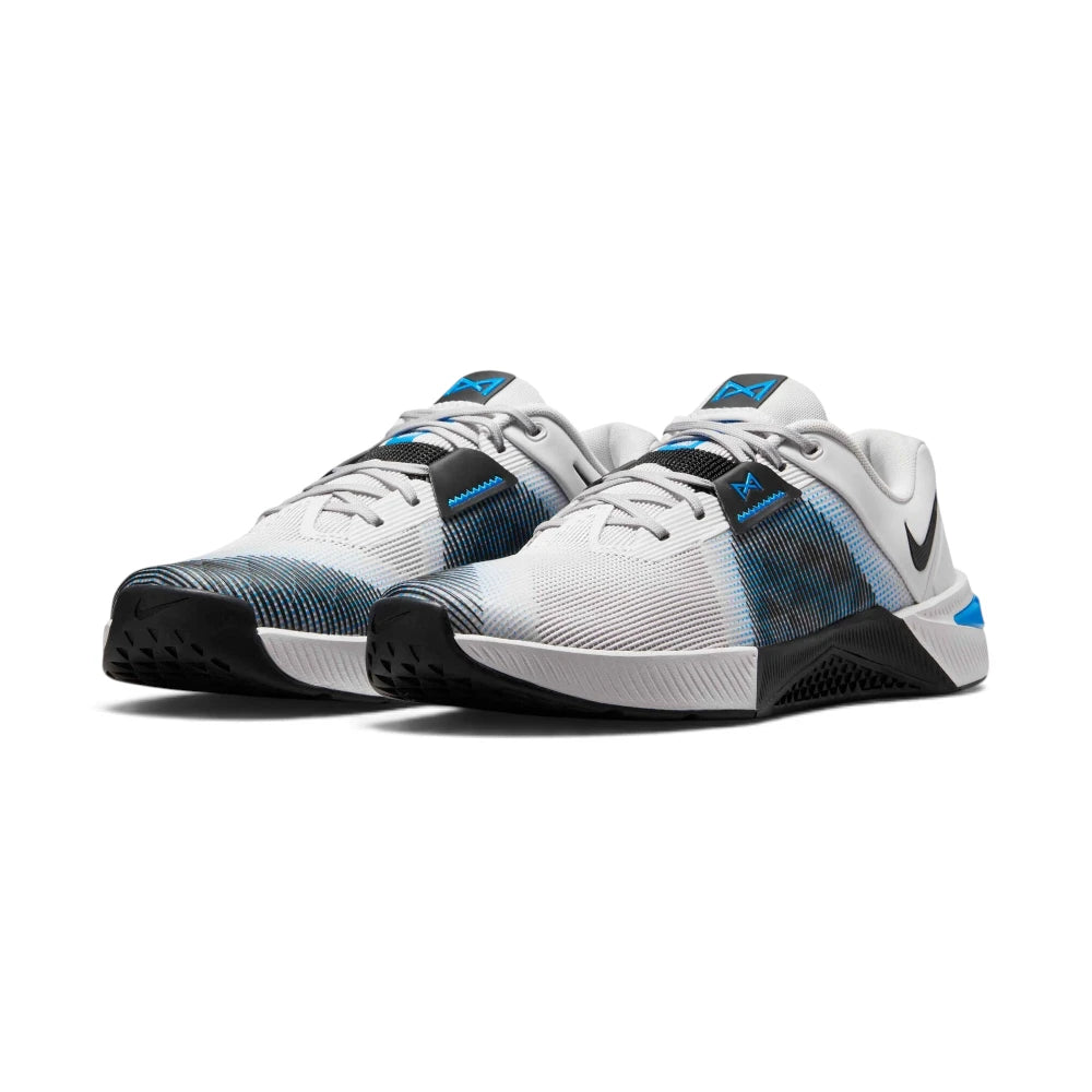 Front three-quarter perspective of both shoes side by side, highlighting the light grey engineered mesh upper, black textured side wall wraps, blue lace-lock details, black toe guards, and white midsoles with blue heel highlights.