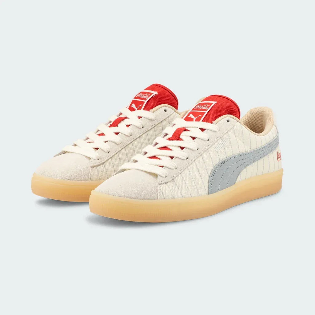 Angled view of two Puma Suede x Coca-Cola Unisex trainers in white, beige, and red, side by side, showcasing their iconic collaboration design.
