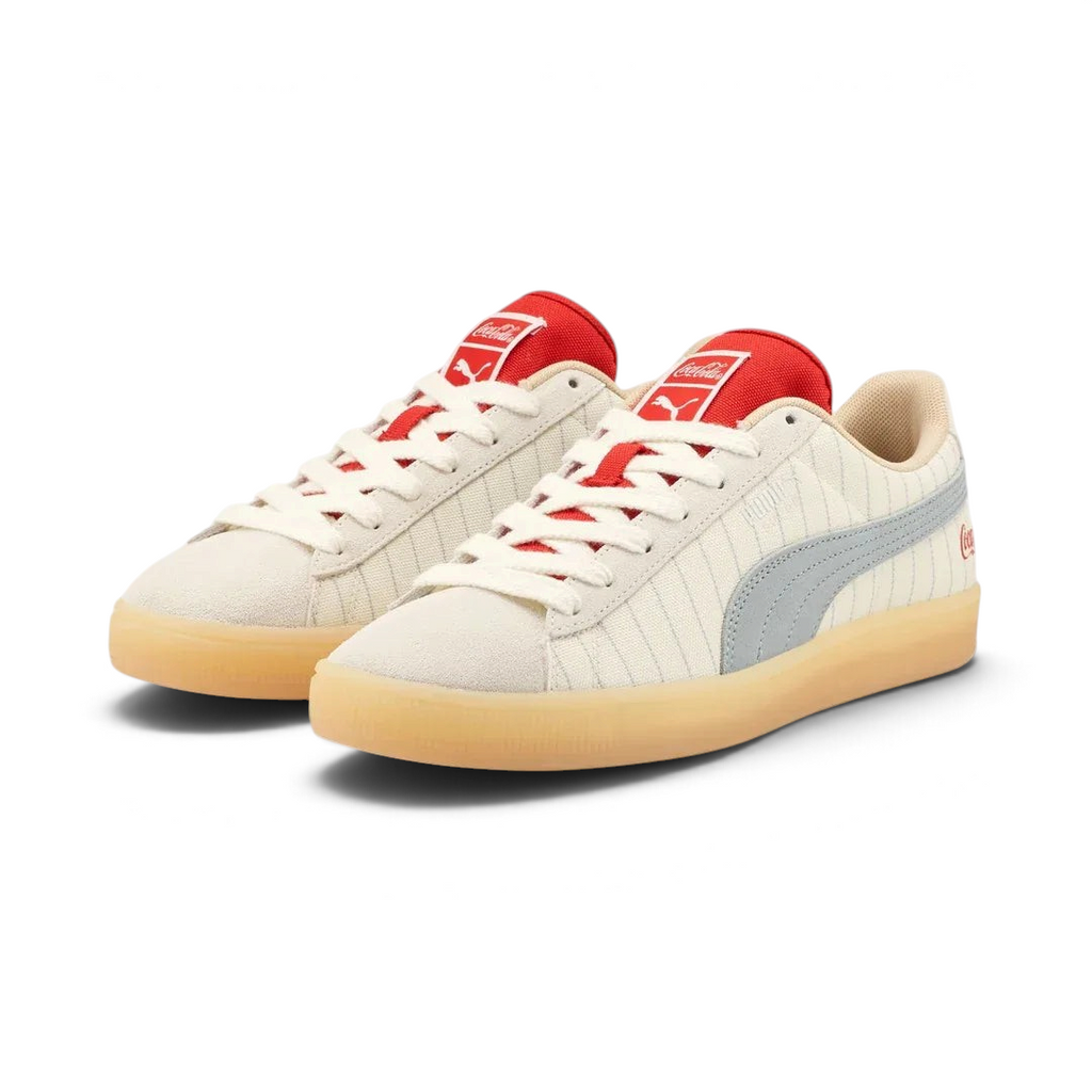 Angled view of two Puma Suede x Coca-Cola Unisex trainers in white, beige, and red, side by side, showcasing their iconic collaboration design.