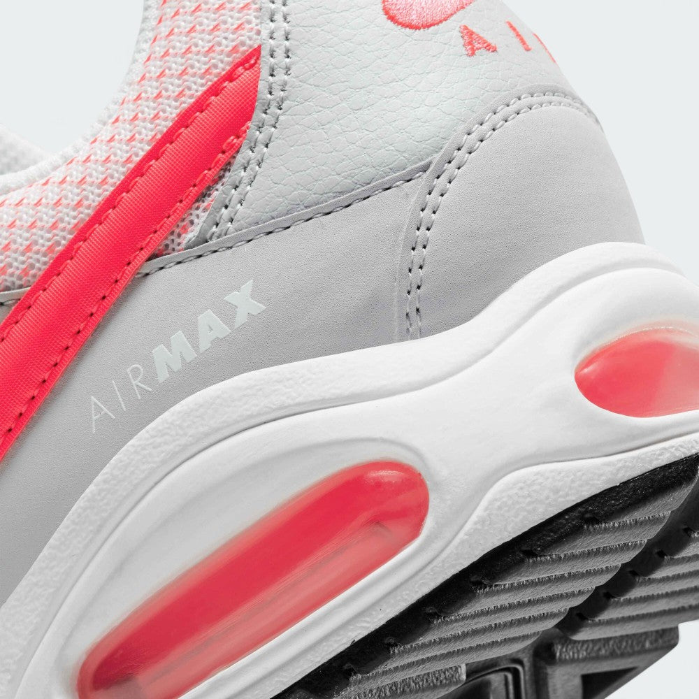 Close-up of a Nike Air Max sneaker in light gray and white with bright pink-red accents, showing the midsole cushioning and textured upper.