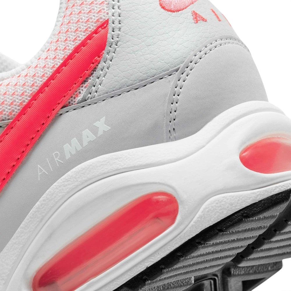 Close-up of a Nike Air Max sneaker in light gray and white with bright pink-red accents, showing the midsole cushioning and textured upper.
